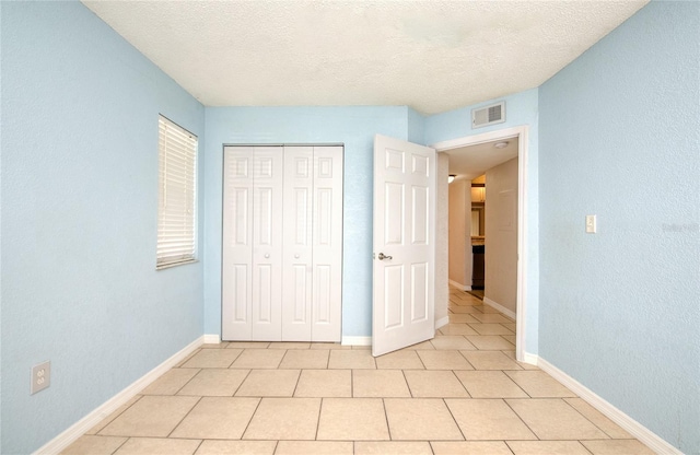 unfurnished bedroom with a closet, a textured ceiling, and light tile patterned flooring