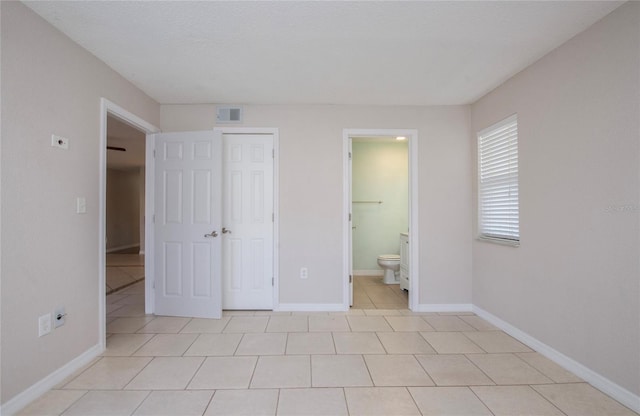 unfurnished bedroom featuring light tile patterned floors, ensuite bath, and a closet