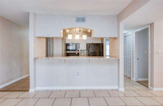 kitchen featuring a breakfast bar, black fridge, light tile patterned floors, kitchen peninsula, and light stone countertops