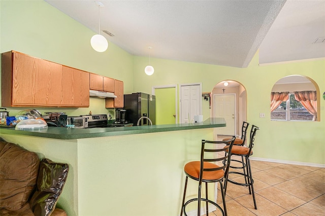 kitchen with light tile patterned flooring, lofted ceiling, a kitchen bar, appliances with stainless steel finishes, and kitchen peninsula