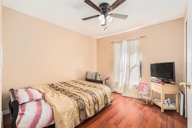 bedroom with ceiling fan, dark wood-type flooring, and a textured ceiling