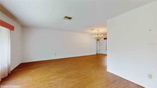 unfurnished room with a textured ceiling, a chandelier, and light hardwood / wood-style floors