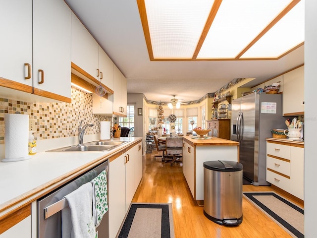 kitchen with light wood-style flooring, a sink, stainless steel appliances, white cabinetry, and tasteful backsplash