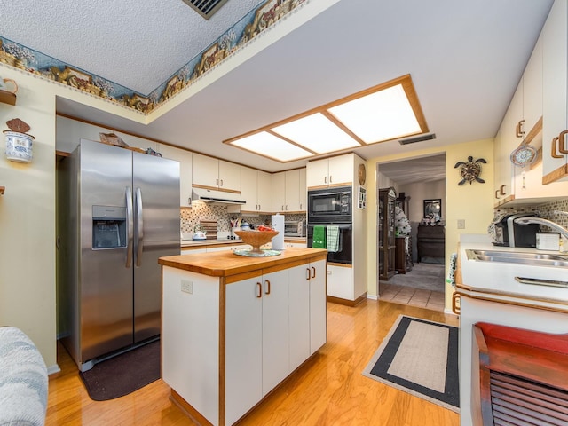 kitchen with under cabinet range hood, butcher block countertops, black appliances, and white cabinetry