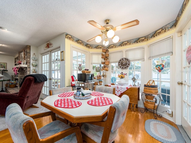 dining space featuring a textured ceiling, light wood-style flooring, ceiling fan, and a large fireplace