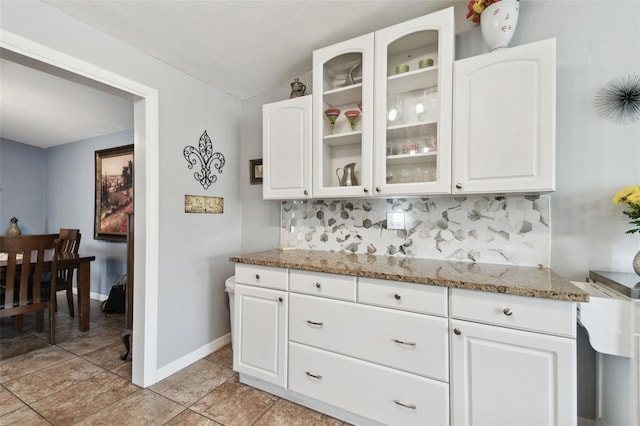 kitchen featuring tasteful backsplash, light stone countertops, and white cabinets