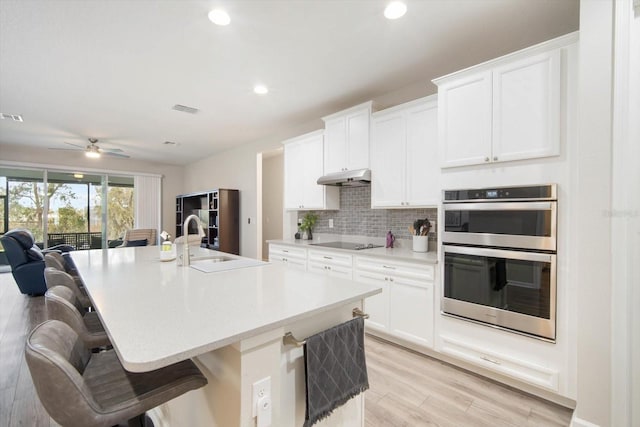 kitchen with under cabinet range hood, a sink, tasteful backsplash, stainless steel double oven, and black electric cooktop