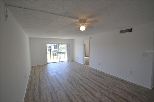 unfurnished room with a textured ceiling, wood finished floors, visible vents, baseboards, and a ceiling fan