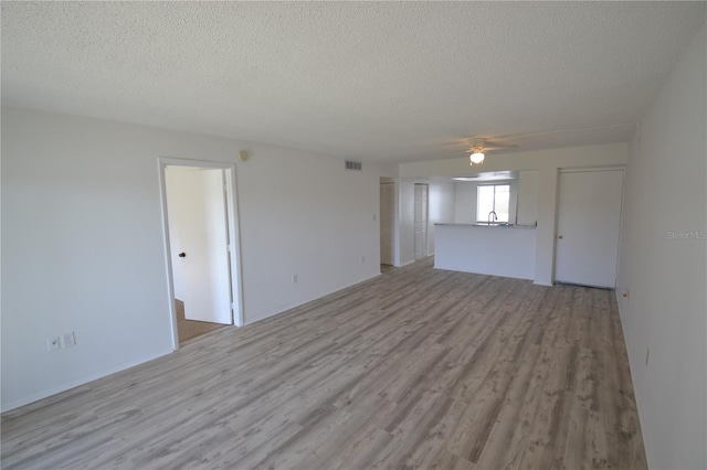 empty room with visible vents, a ceiling fan, a textured ceiling, light wood-style floors, and a sink