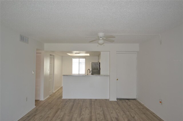 interior space featuring light wood finished floors, visible vents, a ceiling fan, a sink, and a textured ceiling