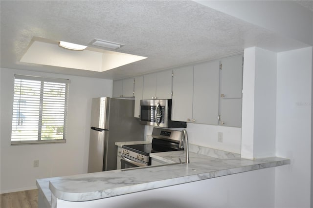 kitchen featuring stainless steel appliances, visible vents, light wood-style floors, a textured ceiling, and a peninsula