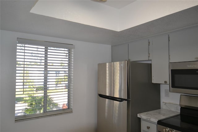 kitchen with appliances with stainless steel finishes, a wealth of natural light, and white cabinetry