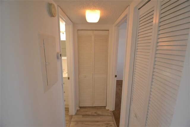 hallway featuring light wood-style floors, electric panel, and a textured ceiling