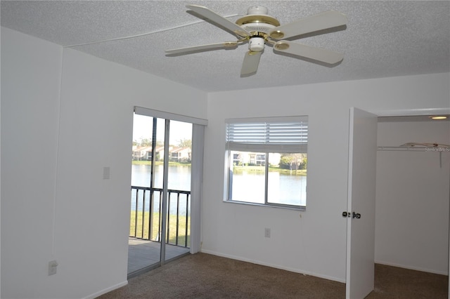 unfurnished bedroom featuring a textured ceiling, access to outside, a water view, and carpet flooring