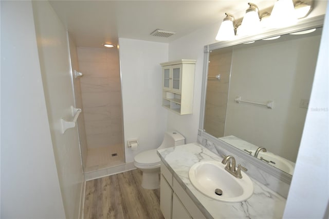 bathroom featuring toilet, wood finished floors, vanity, visible vents, and tiled shower