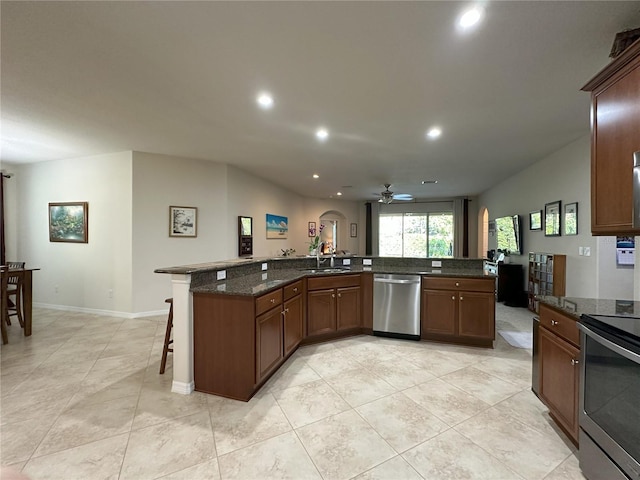 kitchen featuring sink, dark stone countertops, appliances with stainless steel finishes, a kitchen breakfast bar, and ceiling fan