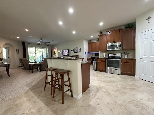 kitchen featuring tasteful backsplash, a kitchen breakfast bar, a kitchen island with sink, light colored carpet, and stainless steel appliances