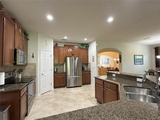 kitchen featuring sink, light tile patterned floors, appliances with stainless steel finishes, dark stone countertops, and tasteful backsplash