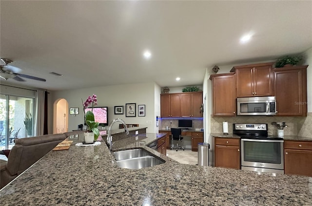 kitchen featuring sink, backsplash, dark stone counters, ceiling fan, and stainless steel appliances