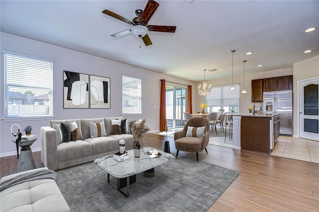 living room with sink, ceiling fan with notable chandelier, a wealth of natural light, and light hardwood / wood-style floors