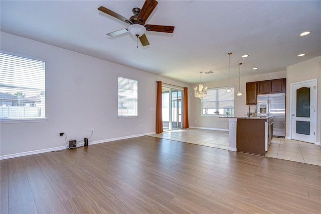 unfurnished living room featuring ceiling fan with notable chandelier, sink, light hardwood / wood-style floors, and a wealth of natural light