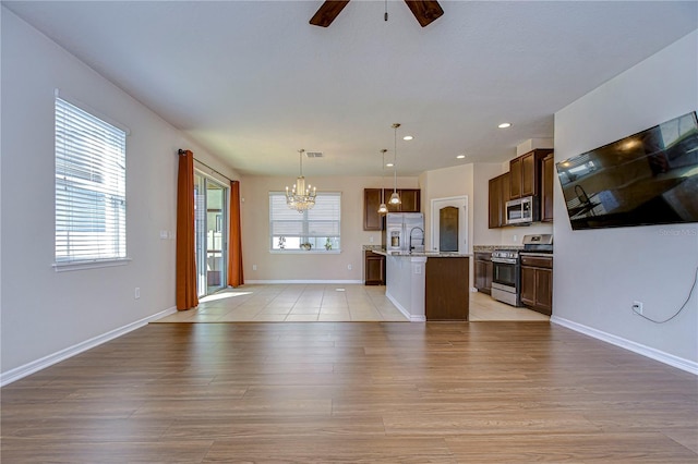 kitchen with hanging light fixtures, light hardwood / wood-style flooring, appliances with stainless steel finishes, a kitchen island with sink, and ceiling fan with notable chandelier