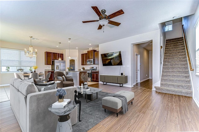 living room featuring ceiling fan with notable chandelier, light hardwood / wood-style floors, and a textured ceiling