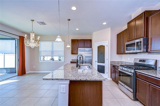 kitchen with appliances with stainless steel finishes, pendant lighting, an island with sink, sink, and light tile patterned floors