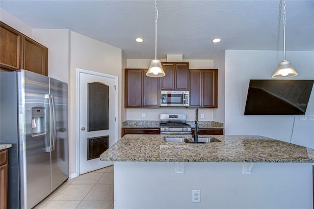 kitchen with stainless steel appliances, hanging light fixtures, light tile patterned floors, and stone counters