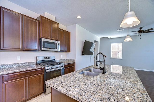 kitchen with appliances with stainless steel finishes, sink, a center island with sink, and light stone counters