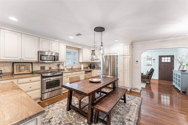 kitchen featuring pendant lighting, hardwood / wood-style flooring, stainless steel appliances, tasteful backsplash, and white cabinets