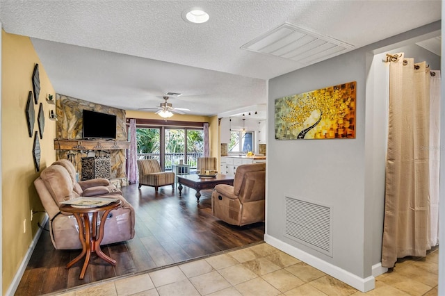 tiled living room featuring ceiling fan, a fireplace, and a textured ceiling