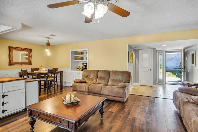 living room featuring ceiling fan, hardwood / wood-style floors, built in features, and a textured ceiling