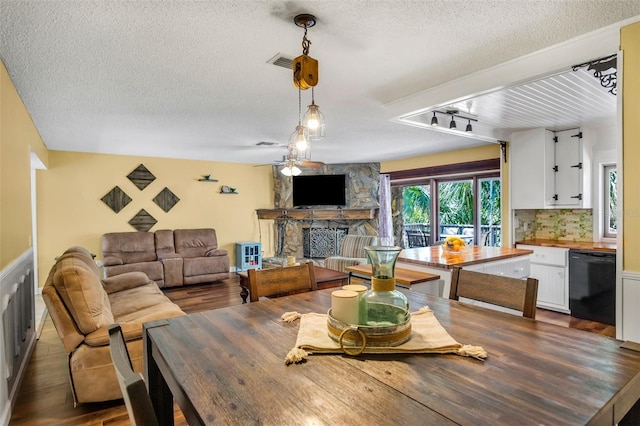 dining space with a stone fireplace, rail lighting, a textured ceiling, dark hardwood / wood-style floors, and ceiling fan