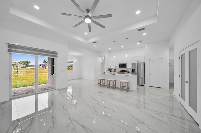 living room with ceiling fan, a tray ceiling, and a high ceiling