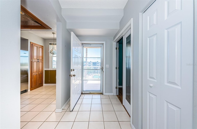 doorway to outside with light tile patterned floors, a textured ceiling, a notable chandelier, and baseboards