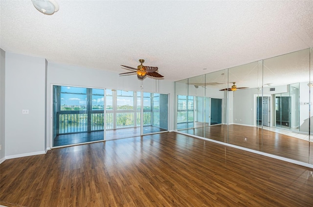 empty room with a textured ceiling, wood finished floors, a ceiling fan, and baseboards