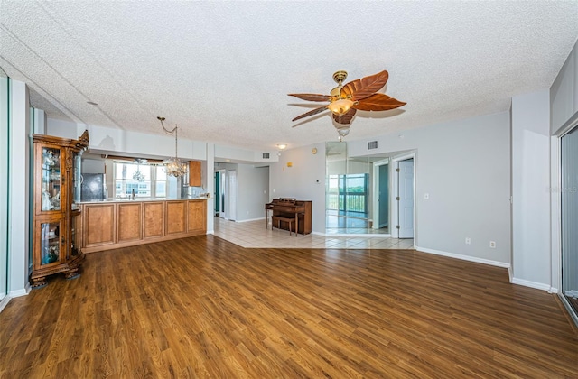 unfurnished living room featuring dark wood-type flooring, a wealth of natural light, and ceiling fan with notable chandelier