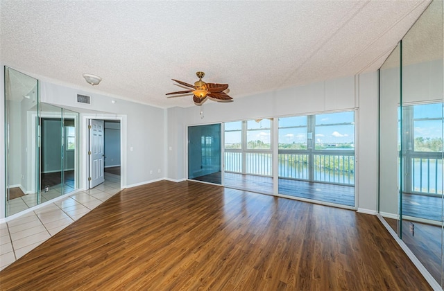 empty room featuring a water view, a textured ceiling, visible vents, and wood finished floors