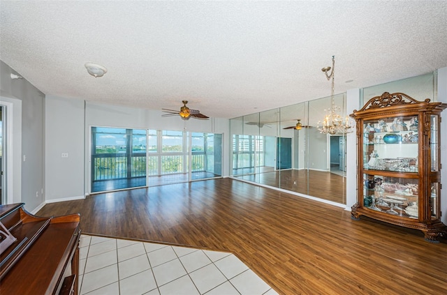 unfurnished living room with a wealth of natural light, wood finished floors, a textured ceiling, and ceiling fan with notable chandelier