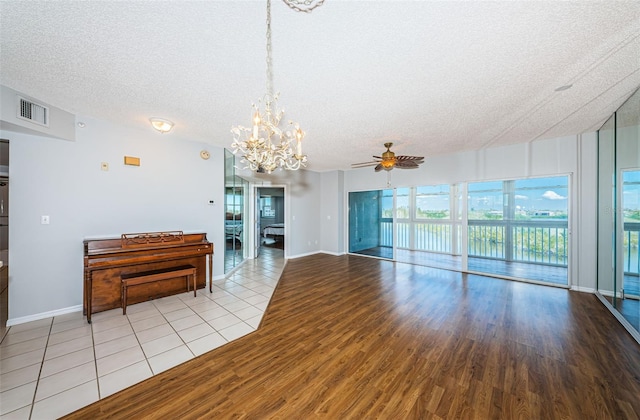 unfurnished living room with a textured ceiling, baseboards, wood finished floors, and ceiling fan with notable chandelier