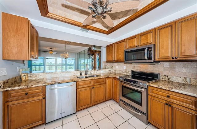 kitchen featuring brown cabinetry, stainless steel appliances, a sink, and a raised ceiling