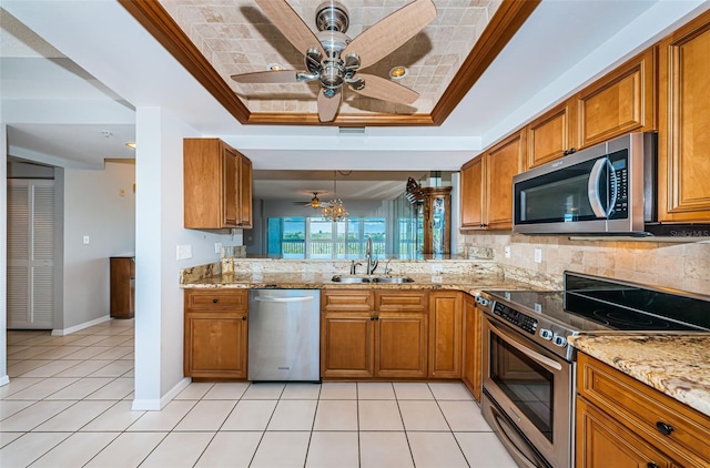 kitchen featuring brown cabinetry, a tray ceiling, stainless steel appliances, and a sink