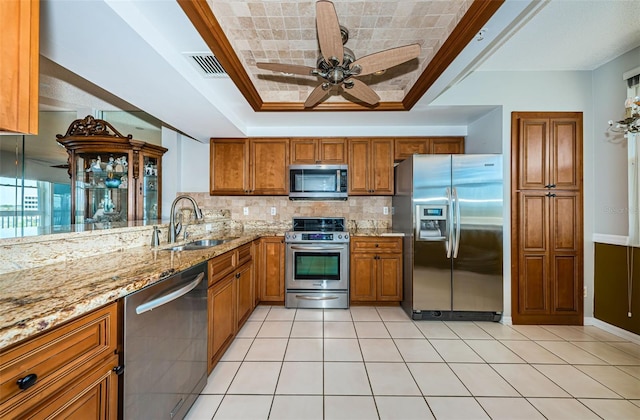 kitchen featuring stainless steel appliances, a raised ceiling, visible vents, brown cabinetry, and a sink