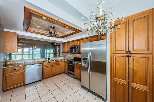 kitchen with brown cabinets, a tray ceiling, stainless steel appliances, and a sink