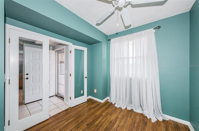 empty room featuring a textured ceiling, ceiling fan, wood finished floors, and baseboards