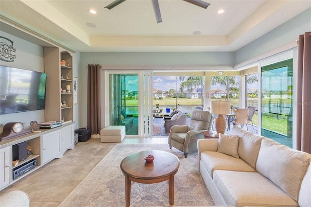 living room featuring ceiling fan, a raised ceiling, built in features, and a wealth of natural light