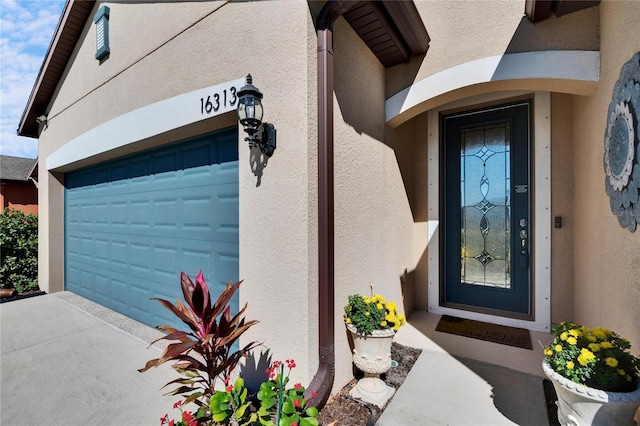 view of exterior entry with a garage, driveway, and stucco siding