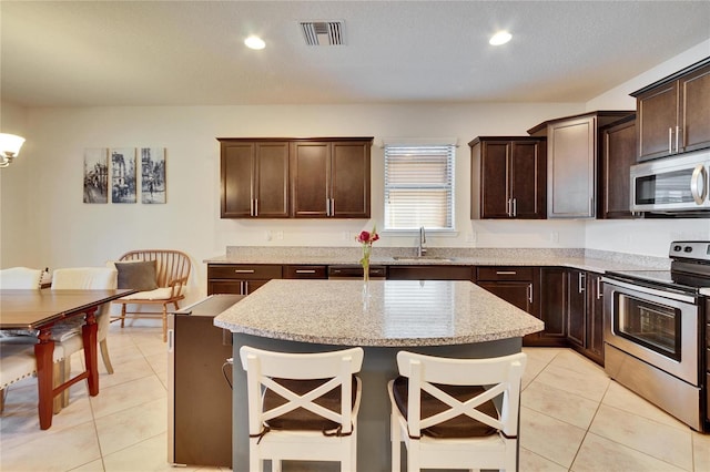 kitchen with visible vents, light stone counters, a center island, stainless steel appliances, and a sink