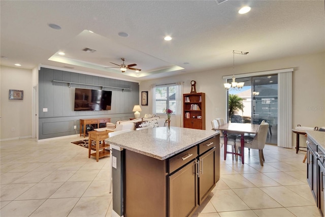 kitchen with light tile patterned floors, visible vents, a kitchen island, a tray ceiling, and pendant lighting